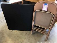 Black folding card table folded and two vintage Samsonite metal folding chairs stacked showing wear.