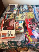 Lot of various vintage board games and playsets on bed, showing box covers and titles including Scrabble for Juniors and Playskool Lincoln Logs.