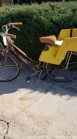 Side profile of the brown Huffy Sierra bicycle showing orange handle grips, brown saddle seat, and yellow child's seat attached over rear wheel.