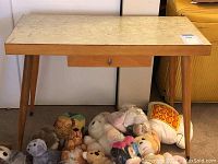 Full view of the mid-century modern wood table with laminate top, tapered legs, and drawer underneath. Stuffed animals are underneath the table but are not included in the lot.