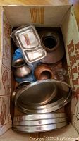 Photo showing multiple metal urns, pots, trays, and vases in a box from a top view. Includes oval trays at the front and several urns/pots with patina.