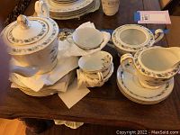 Porcelain Noritake coffee or tea service set displayed on a wooden table with teapot, cups, saucers, creamer, sugar bowl (lid missing).