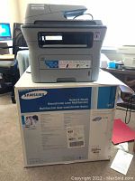 Samsung SCX-426FN monochrome multifunction laser printer shown on top of its original box. Box details indicate network-ready laser multifunction capabilities.