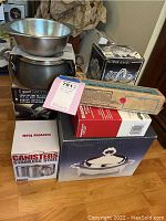 Photo showing stacked mixing bowls, boxes of various kitchen items including silver serving dish, canisters, electric cutting tool, and steak cutters.