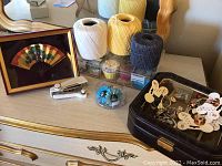 Photo showing sewing threads, beads, pet decorative chains, a framed Asian fan, and a staple gun on a wooden surface.