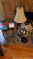 Small round table with floral glass top and two lamps placed by a fireplace.