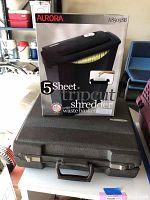 Aurora AS505SB paper shredder box on top of black carrying case, with background showing part of a garage or storage space.