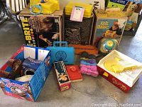 Wide shot showing multiple vintage toys including Lite-Brite box, Magic Knit box, Fisher Price Carrying Case, toy drum and other boxed toys.