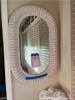 Front view of the white wicker framed mirror hanging on a wall, showing the wicker texture and oval shape.