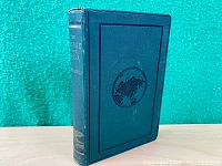 Front cover of the dark blue hardcover book showing embossed world map and ships illustration.