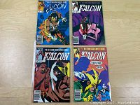 Four comic books in protective sleeves arranged on a wooden surface. Covers feature The Falcon in various action poses with bold comic artwork from Marvel Comics.