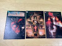 Three comic books from the series laid out flat, showing covers of Book I, II, III respectively.