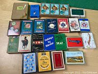 Full assortment of vintage playing card decks arranged on surface, showing about 23 decks in various original boxes.
