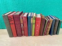 Front view of 14 old hardcover decorative books with colorful spines in various conditions