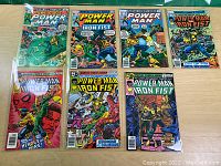 Full view of seven Power Man and Iron Fist comic books laid out on a wooden surface showing front covers.