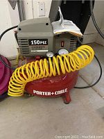 Full view of Porter Cable 150 PSI pancake air compressor with yellow coiled air hose and instructions resting on top.