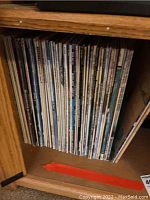 Photo of 33 LP records stored vertically on a wooden shelf, showing spines of various albums in mixture of light and dark covers.