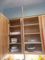 Two kitchen cupboards open showing multiple shelves with baking pans, casserole dishes, mixing bowls.