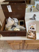 Wooden box containing assorted seashells, some wrapped in bubble wrap and plastic bags.