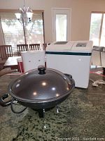 Photo showing the three items: electric wok with lid, bread machine, and coffee pot on kitchen counter.