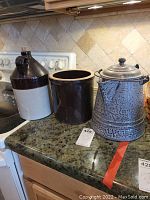 Two stoneware crock pots and a gray enamel metal kettle on kitchen countertop.