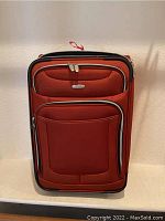 Red rolling luggage with Embark branding and multiple front zip pockets visible from front view