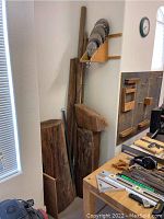 View of large tree trunk portions leaning against wall, dowels behind, circular saw blades mounted on wall rack