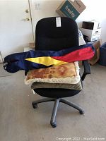 Black office chair with armrests and rolling casters, showing the folded cloth chair and two pillows placed on the seat.