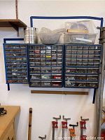 Wide shot of three blue plastic wall-mounted organizer bins filled with various hardware items in transparent drawers