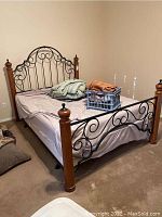 Angled view of queen bed frame with mattress, linens and decorative scrollwork