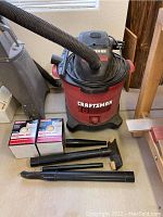 Full view of Craftsman 16 gallon wet/dry vacuum cleaner with hose attached and accessories including hose-ended nozzles and two boxes with extra filters.