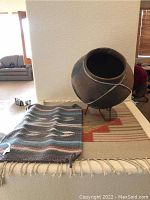Photo of large southwest pottery pot on metal stand and two small wool blankets beneath it.