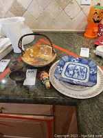 Lot of vintage ceramic plates, bowls, and a decorative cork stopper displayed on a counter.