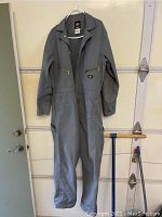 Full view of the gray Dickies work overall hanging showing front zipper and long sleeves.