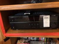 Full view of Yamaha receiver on shelf, showing front panel controls and display with remote control on top.