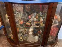 Full view of the glass wooden display cabinet showing assorted mini egg figurines and decorative collectibles inside on two glass shelves.