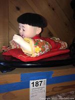 Porcelain doll with black hair in floral orange kimono-style garment on a red cushion