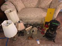 Assorted table lamps, lanterns, oil lamps and faux stove arranged on floor