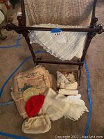 Wooden stand with assorted linens draped and a box holding various crochet and lace items, red knit cap, small handbag visible.