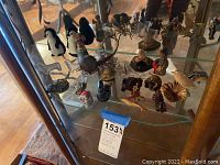 Photo of glass shelf displaying assorted small animal figurines and tea cup holders needing cleaning.