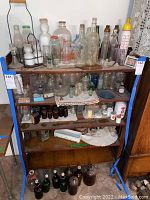 Full view of wooden shelf holding assorted vintage glass bottles, jars, salt and pepper shakers, baby bottle, and decorative glass items.
