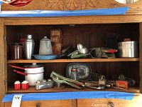 Wide view of wooden shelf unit with assorted vintage kitchen items: enamelware pots, cocktail shaker, coffee pot, bread tray, vintage tins, and kitchen utensils.