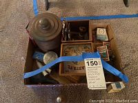 Overview of assortment of vintage smoking and tobacco-related items in a cardboard box including metal containers, tins, pipes, matchboxes, and decor
