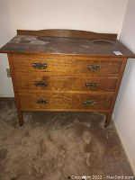 Front full view of oak wood side bed table with three metal handled drawers and dusty top surface.