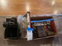 Overview of the lot showing both the vintage binoculars in leather case and the black film projector with attached motor inside open carrying cases.