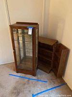 Photo showing both curio cabinet with glass door and shelves and adjacent wooden storage cabinet with door open.