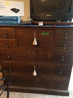 Front view of 8 drawer oak dresser with two tassel keys and metal pull handles. Various items on top including a TV and boxes.
