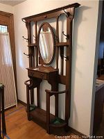 Front view of the wooden entry coat tree showing oval mirror, hooks, drawers, umbrella stands, and lower shelf.