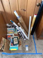 Overview of books stacked on floor with multiple rolled posters or prints in tubes leaning against the wall.