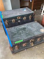 Photo showing two vintage steamer trunks closed, visible metal hardware and riveted edges.